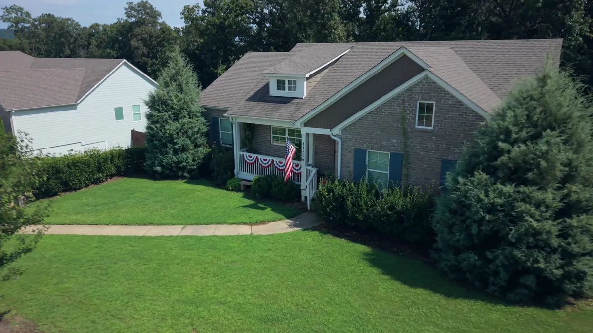 Elevated front view of a brick craftsman home with mature evergreens and a manicured lawn