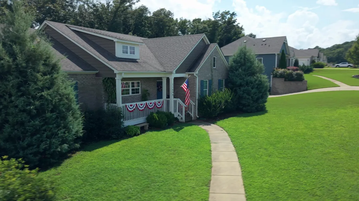 Low aerial approach along the front walkway to a brick craftsman home with a flag on the porch